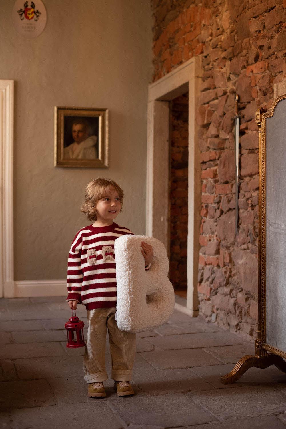 Boucle letter cushion B Teddy pillow by bettys home held by Young boy with red stipe sweater in hands 