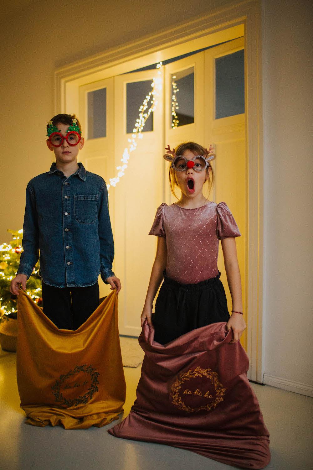 two kids during christmas eve standing with christmas sack in yellow and pink by Bettys Home 
