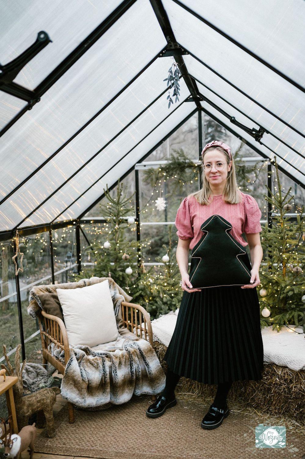 Young woman standing in greenhouse with christmas tree pillow in hear hands. christmas decorations for bedroom 