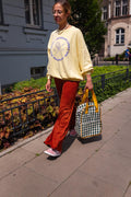 Young woman on her walk in city held green gingham backpack by Bettys home in her hand