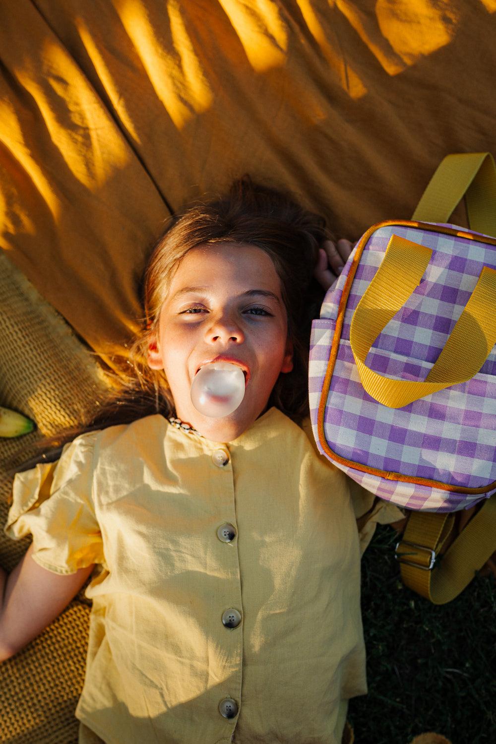 cute girl on yellow blanket with small checkered backpack. Gingham retro backpack