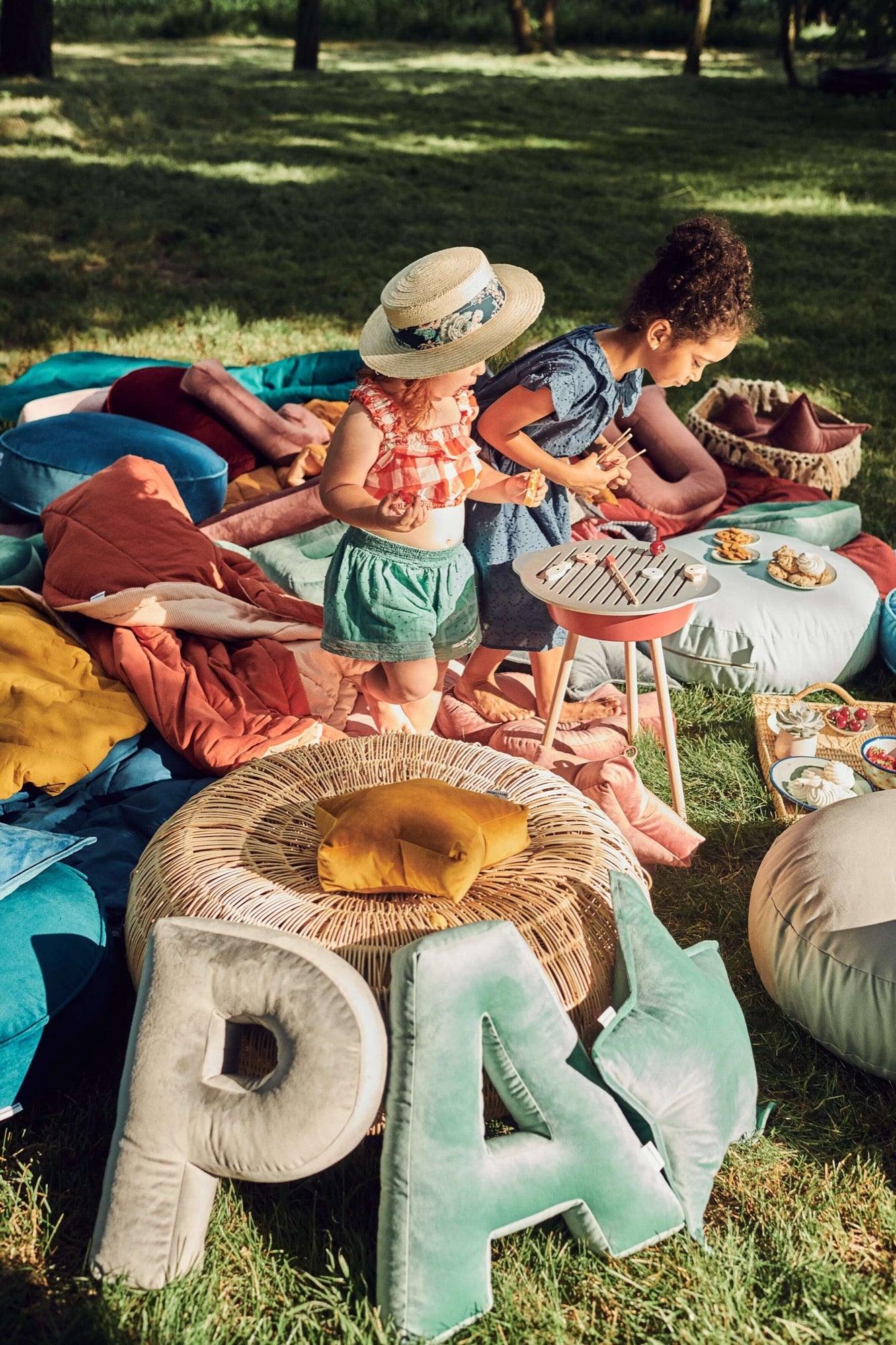 two little girls playing in garden at front of them are two velvet letter cushions P and A by bettys home 