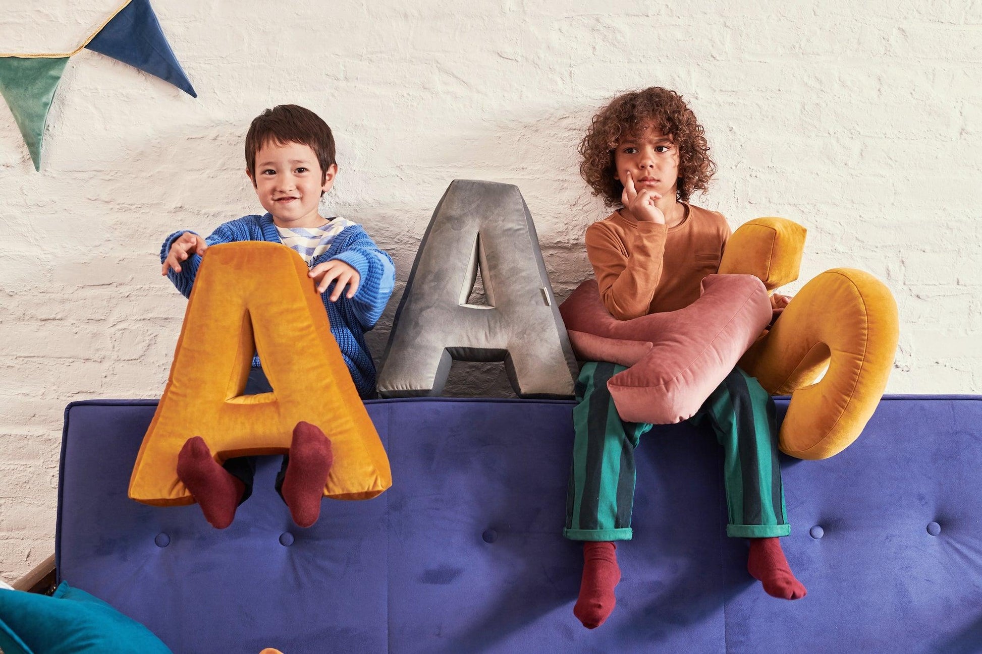 two young boys sitting on sofa with velvet letter shaped cushions a and s in yellow by bettys home