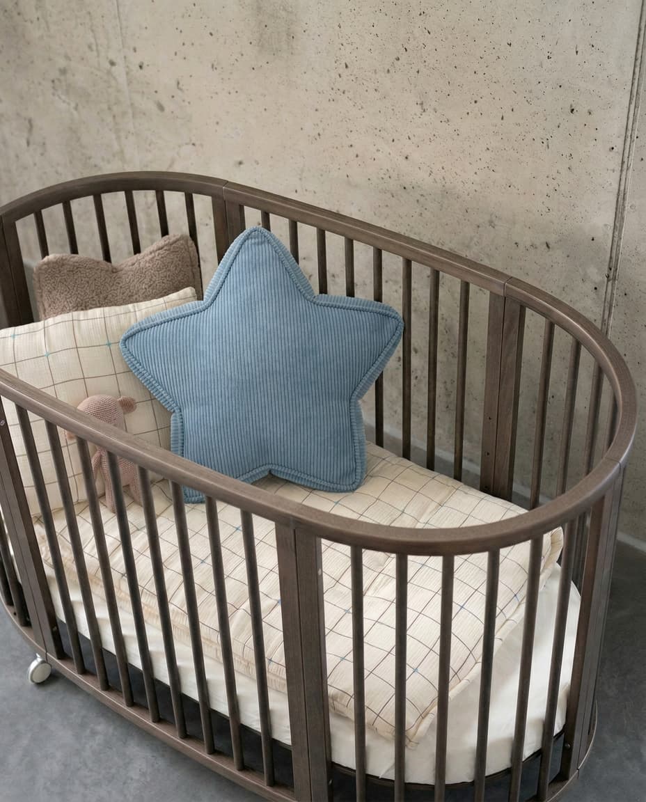 Blue corduroy star cushion styled in oval wooden crib against concrete wall by Bettys Home