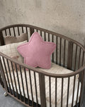 Pink corduroy star cushion styled in oval wooden crib against concrete wall by Bettys Home