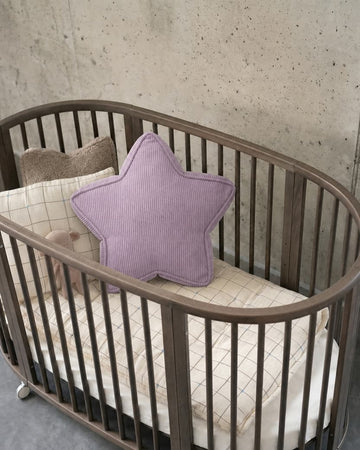 Lavender corduroy star cushion styled in oval wooden crib against concrete wall by Bettys Home