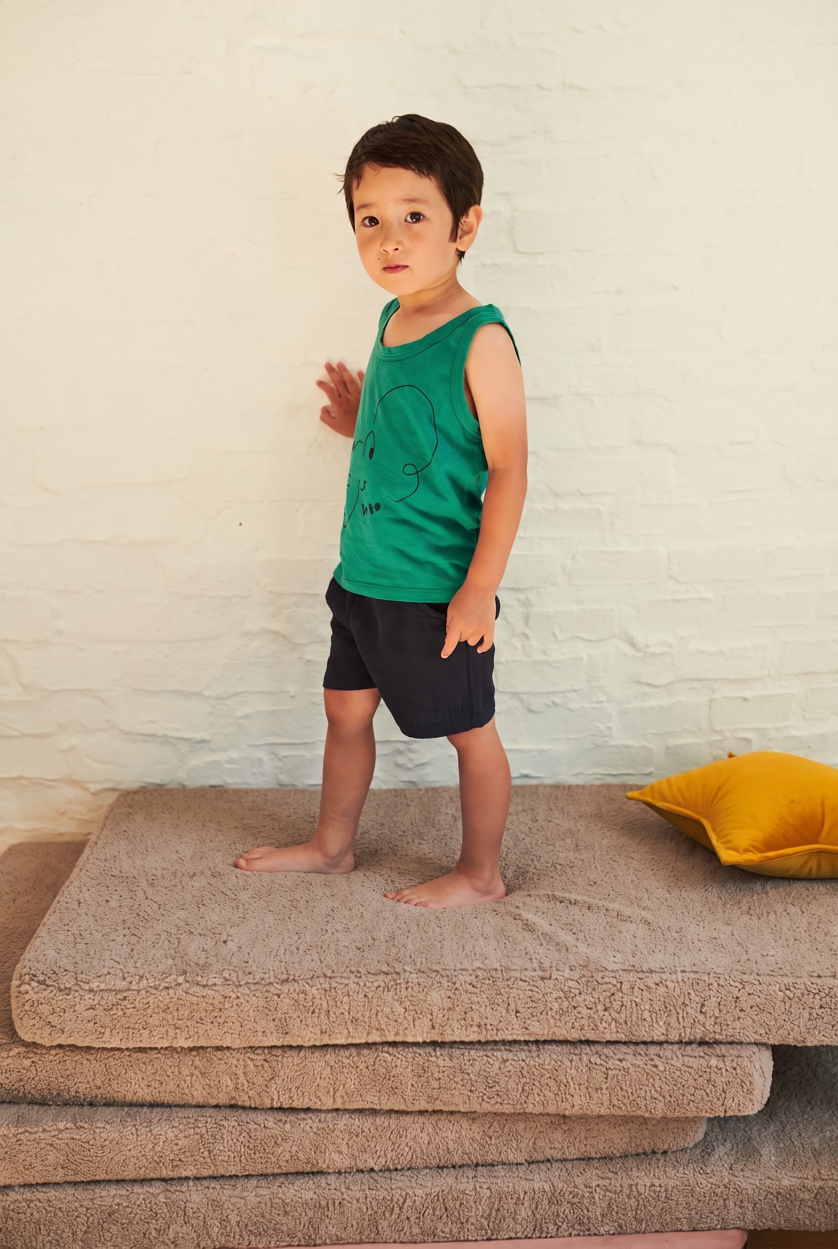Little boy standing on stacked mocha bouclé floor mattresses in a bedroom – by Bettys Home