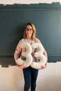 Young woman holding boucle number cushions 33 by bettys home in front of grey wall