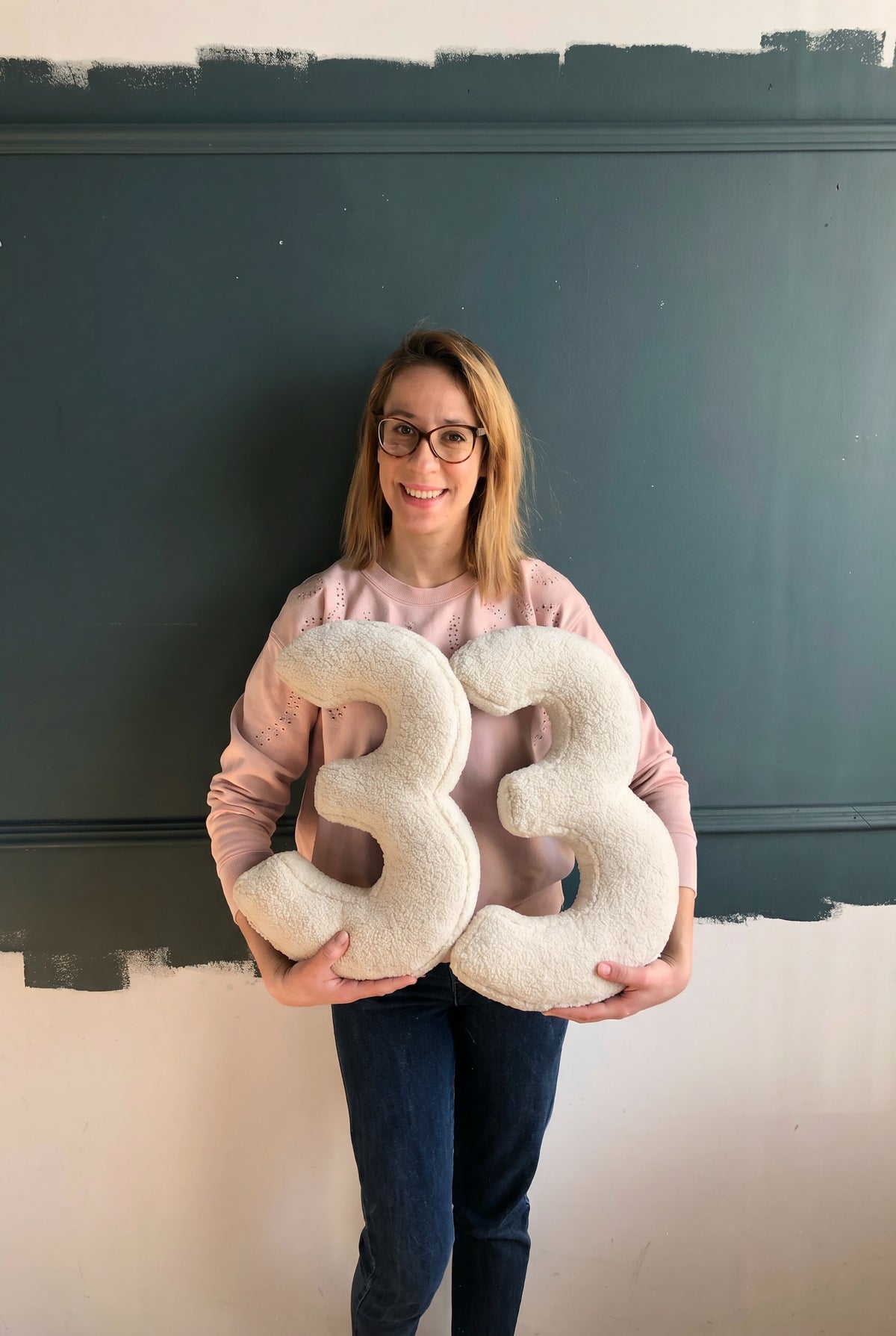Young woman holding boucle number cushions 33 by bettys home in front of grey wall