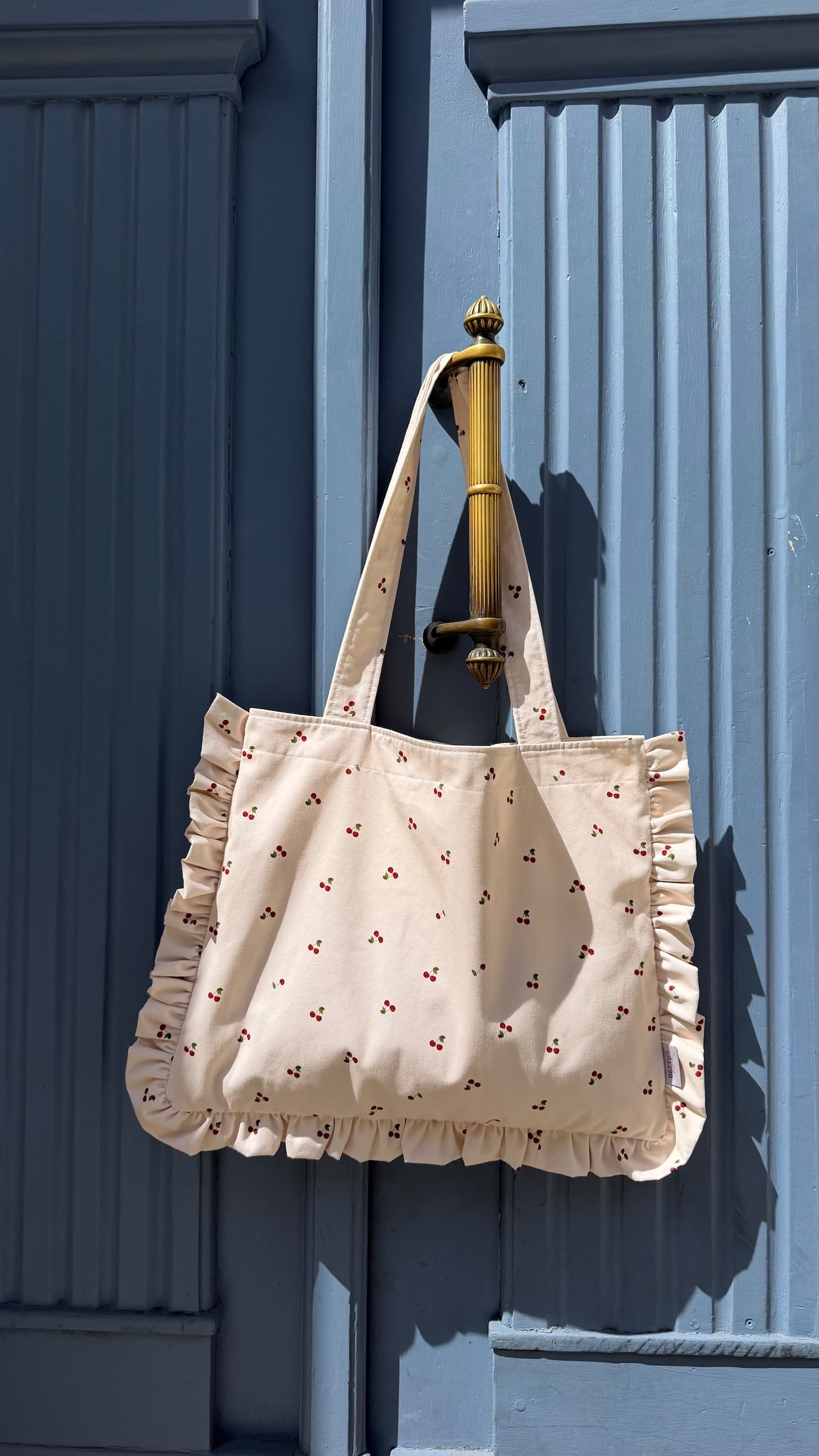 cotton tote bag with ruffle by Bettys home hanging on blue doors