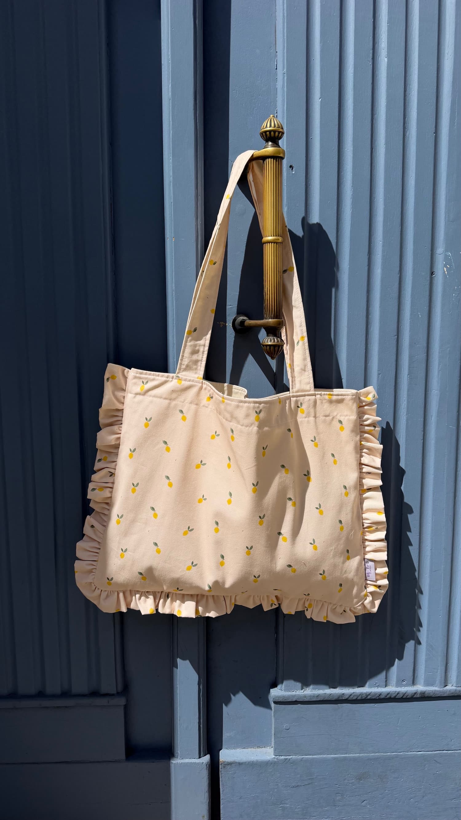 cotton tote bag with ruffle by Bettys home and lemon print hanging on blue doors