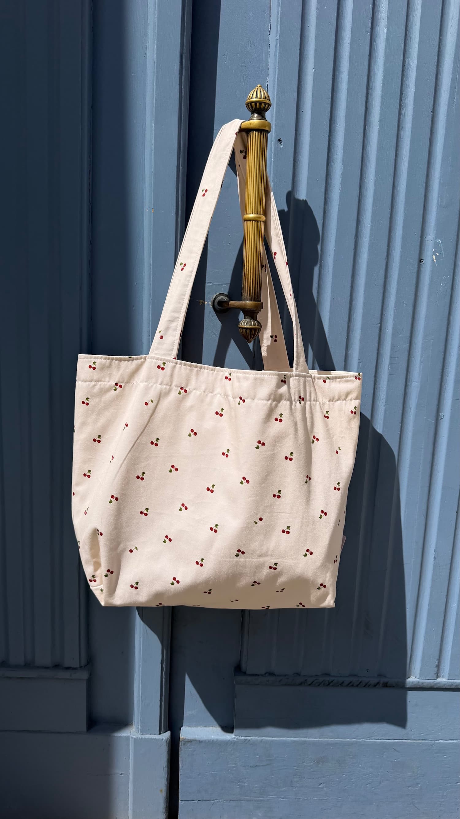 cotton tote bag with ruffle by Bettys home and cherry print hanging on blue doors