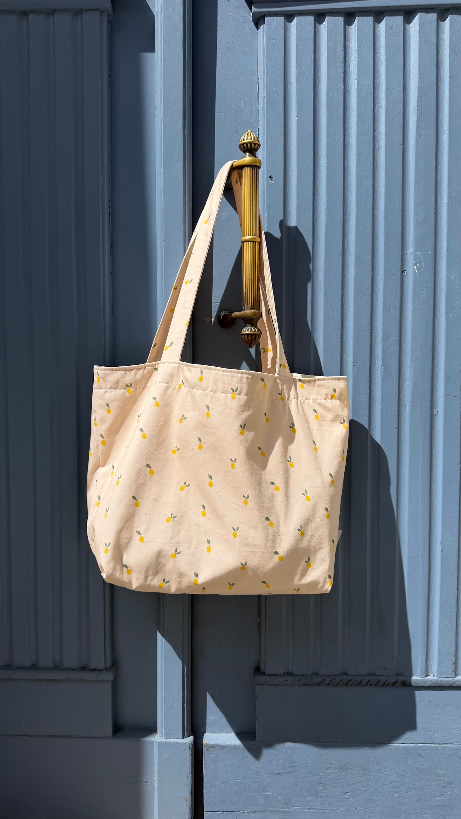cotton tote bag with ruffle by Bettys home and lemon print hanging on blue doors